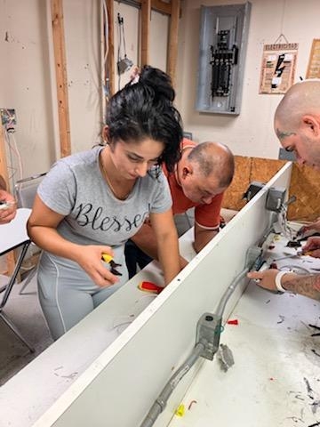 Curso de Electricidad en Español – ITA Estudiantes del curso de Electricidad de ITA realizando conexiones eléctricas en práctica de aula.