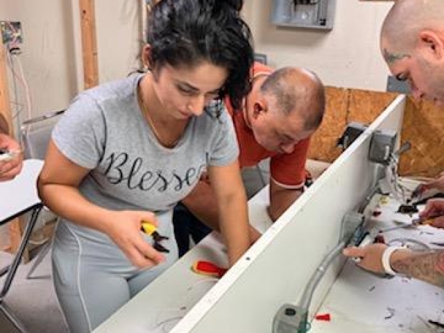 Curso de Electricidad en Español – ITA Estudiantes del curso de Electricidad de ITA realizando conexiones eléctricas en práctica de aula.