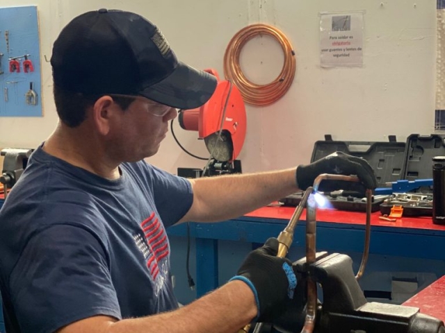 Alumno realizando soldadura en componentes HVAC durante curso técnico de ITA.
