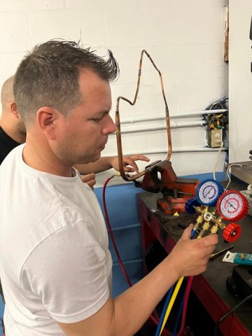 Uso de manómetros en sistemas de aire acondicionado – ITA Estudiante midiendo presión con manómetros en práctica de aire acondicionado en ITA.