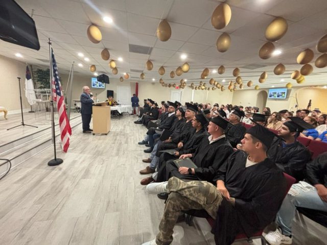 Graduación del Instituto Tecnológico Americano Ceremonia de graduación del Instituto Tecnológico Americano con estudiantes vestidos con toga y birrete escuchando el discurso en el auditorio.