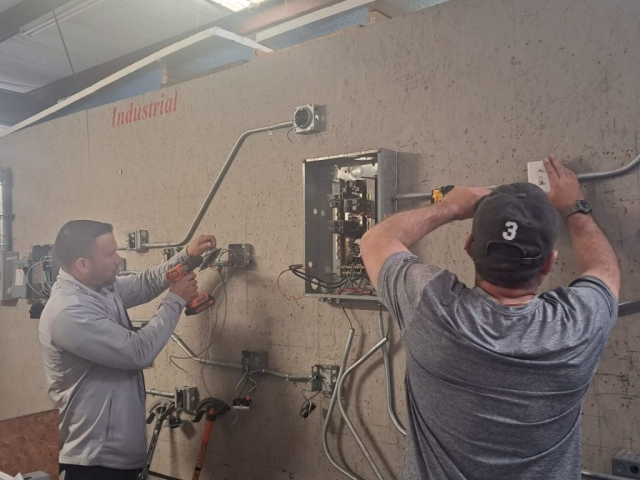 Estudiantes del ITA Columbus realizando prácticas de electricidad industrial con paneles y conduits.